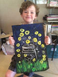 a young boy holding up a painting in front of his face and smiling at the camera