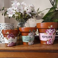 three flower pots sitting on top of a wooden table next to a vase filled with flowers