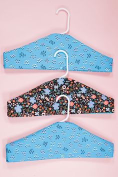 two blue hangers with flowers on them against a pink background, one has an umbrella