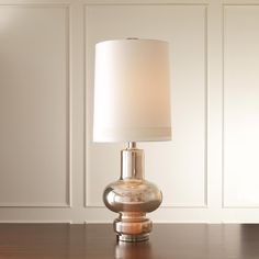 a lamp on a table in front of a white wall and wooden floor with paneled walls