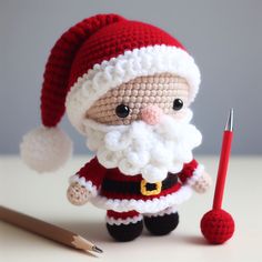 a crocheted santa clause doll next to a pencil