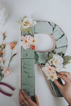 two hands are working on the letters made out of wood and paper flowers with scissors