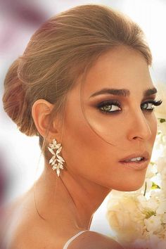 a woman with flowers in her hair and makeup is looking at the camera while wearing large earrings