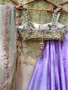 A three-piece tea green and lavender mirror lehenga set from the Priti Sahni collection. This beautiful raw silk lavender lehenga with floral mirror hand embroidery belt detail is paired with a tea green mirror bustier in sequin, beads, and mirror multi-hued hand embroidery. The lehenga has side hanging ball tassels to the waistline. And the blouse has thread-sequins tassel tie-up at the back. This outfit is completed with a tea green tulle mirror work net dupatta with scalloped edging. Purple Anarkali Pre-draped Saree With Mirror Work, Bollywood Style Lavender Sharara With Mirror Work, Festive Lavender Sets With Mirror Work, Purple Dola Silk Lehenga With Gota Work, Party Lehenga With Mirror Work In Lavender, Lavender Lehenga With Mirror Work For Party, Party Lavender Lehenga With Mirror Work, Traditional Lavender Sets With Mirror Work, Lavender Mirror Work Choli For Party