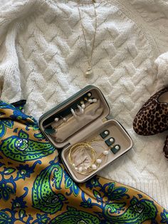 an open suitcase sitting on top of a bed next to some shoes and bracelets