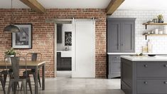 a brick wall in a kitchen with grey cupboards and wooden table, gray chairs