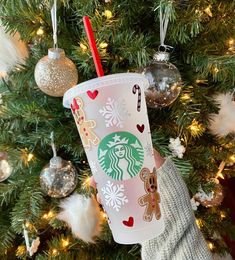 someone holding up a starbucks cup in front of a christmas tree with ornaments on it