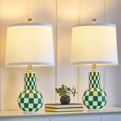 two green and white checkered vases sitting on top of a dresser next to a lamp