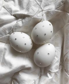 three white eggs sitting on top of a bed covered in white sheets with silver dots