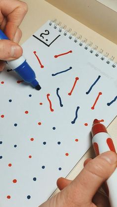 a person is writing on a calendar with blue marker and red dot markers in front of them