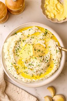 mashed potatoes in a white bowl with butter and seasoning on the side next to other ingredients