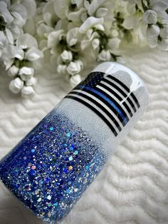 a blue and silver glitter bottle sitting on top of a white blanket next to flowers