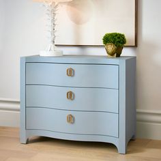 a blue dresser with two drawers and a plant on top in front of a painting