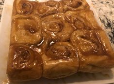 a square white plate with cinnamon rolls covered in caramel icing on a marble counter top