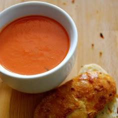 a bowl of tomato soup next to a piece of bread