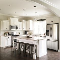 an open kitchen with white cabinets and stainless steel appliances, along with bar stools