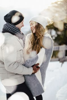 a man and woman standing in the snow with their arms around each other, smiling