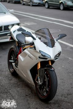 a white motorcycle parked on the side of the road next to a silver and black car