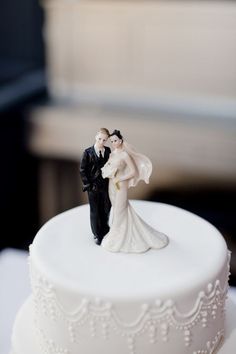 a bride and groom figurine on top of a wedding cake with white frosting