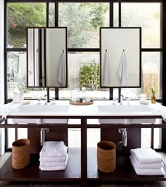 a bathroom with two sinks, mirrors and towels on the counter top in front of large windows