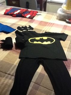 a batman shirt laying on top of a bed next to other clothing and shoes in a room