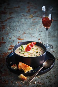 a bowl of soup with bread and garnish next to a glass of wine