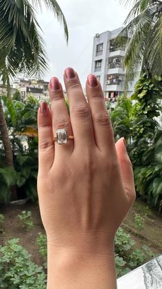 a woman's hand with a ring on it and palm trees in the background