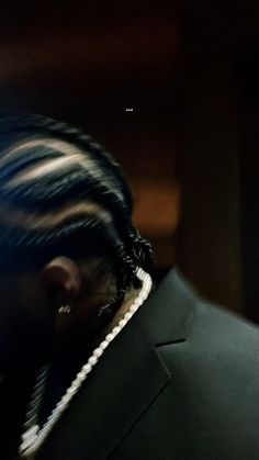 a man with dreadlocks wearing a black suit and pearls on his neck is looking off into the distance