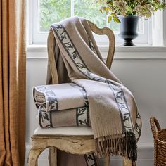 a chair sitting next to a window with a blanket on top of it and a vase filled with flowers