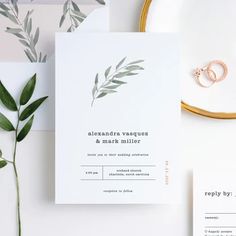 the wedding stationery is laid out on a table next to some greenery and rings