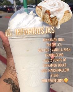 a person holding up a drink with whipped cream and cinnamon rolls on the top, in front of a parking lot