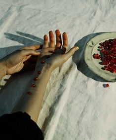 two hands reaching for some food on a white table cloth next to a plate with red berries