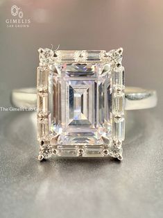 an emerald cut diamond ring with baguetts on the sides and side stones around the band