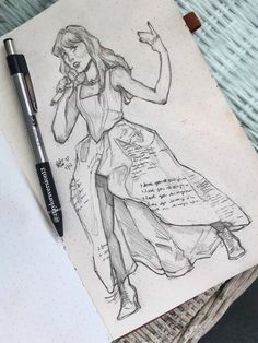 a pencil drawing of a woman in a dress on top of a notebook with a pen next to it