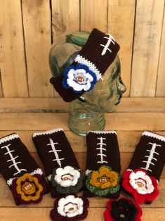 crocheted football mitts with flowers on them sitting in front of a glass vase