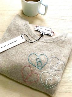 a sweater with embroidered hearts on it next to a cup of coffee and a name tag