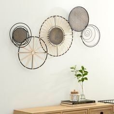 three metal circles hang on the wall next to a dresser with drawers and a plant