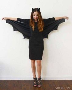 a woman wearing a bat costume standing in front of a wall with her arms outstretched