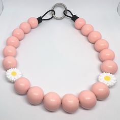 a pink beaded necklace with white flowers and black rubber cord on a white background