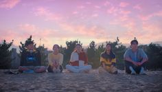 four people sitting on the sand with trees in the background at sunset or sunrise time