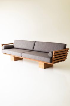 a couch made out of wood and grey fabric on top of a white floor next to a wall