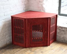 a red dog crate sitting on top of a wooden floor next to a brick wall