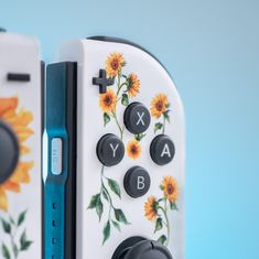 two video game controllers sitting next to each other on a blue surface with sunflowers painted on them