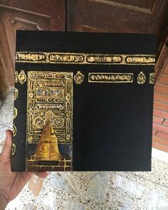 a person holding up a black and gold book in front of a wooden door with ornate designs on it