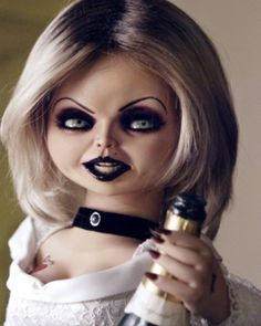 a woman dressed as a doll holding a wine bottle and looking at the camera with evil makeup on her face