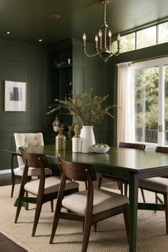 a dining room with green walls and wooden table surrounded by white upholstered chairs