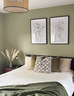 two framed pictures hang above a bed in a bedroom with green walls and white linens