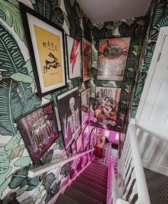 the stairs are lined with posters and pictures on the wall, while another set of stairs leads up to the second floor