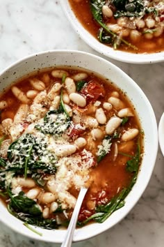 two white bowls filled with beans and spinach on top of a marble countertop