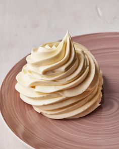 a cupcake with white frosting on a pink plate